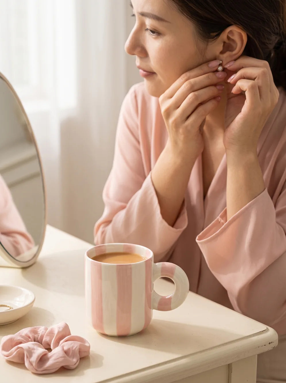A quiet moment at the dressing table, with a pink ceramic mug beside her.