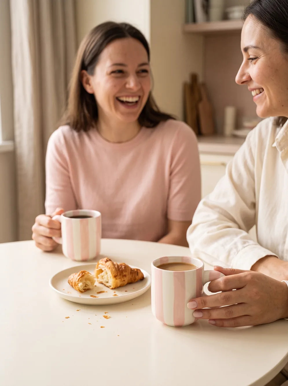 Two women laughing together over coffee and pastries.